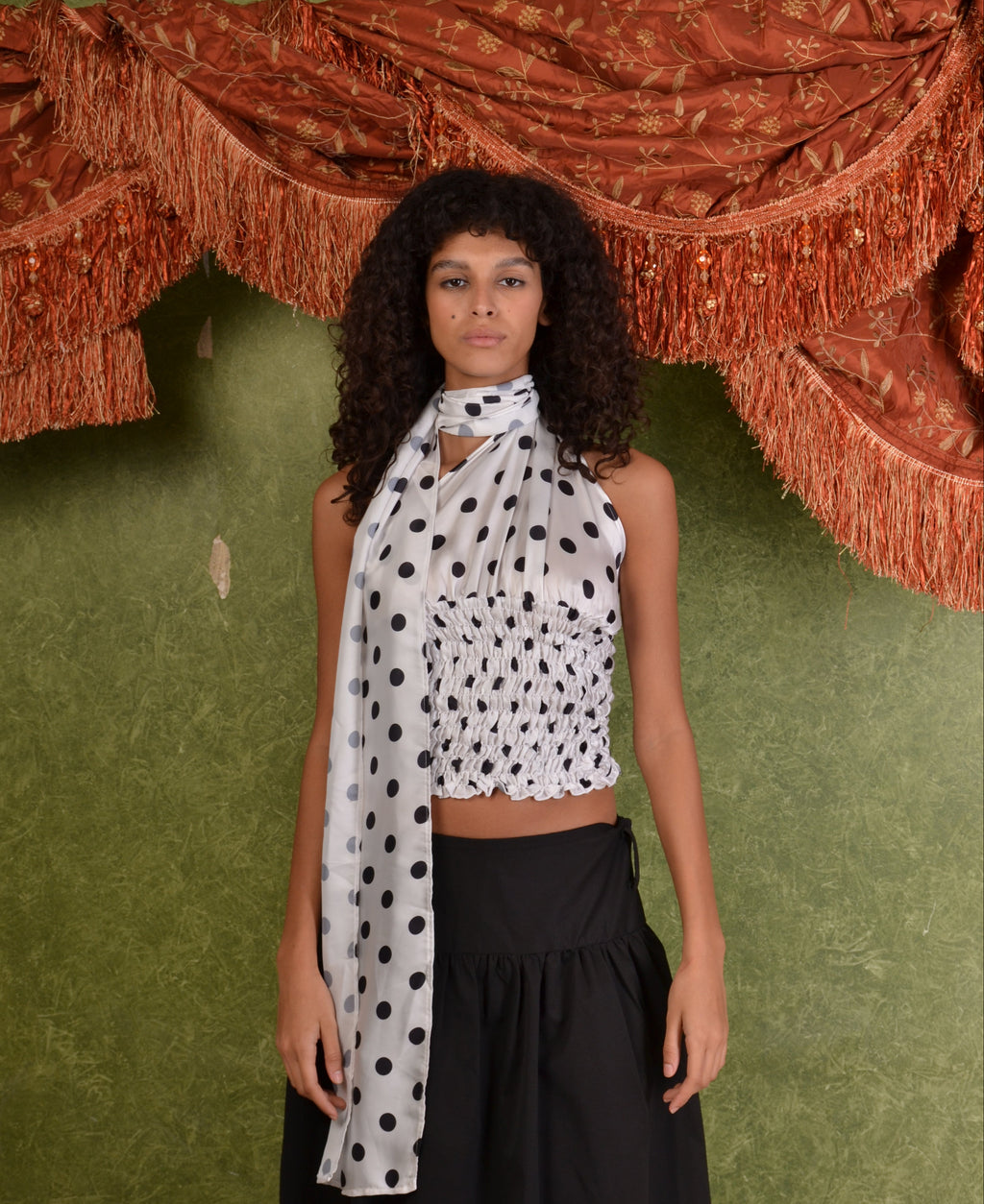 Person wearing a polka dot top and black pants on a green floor with a textured red object.