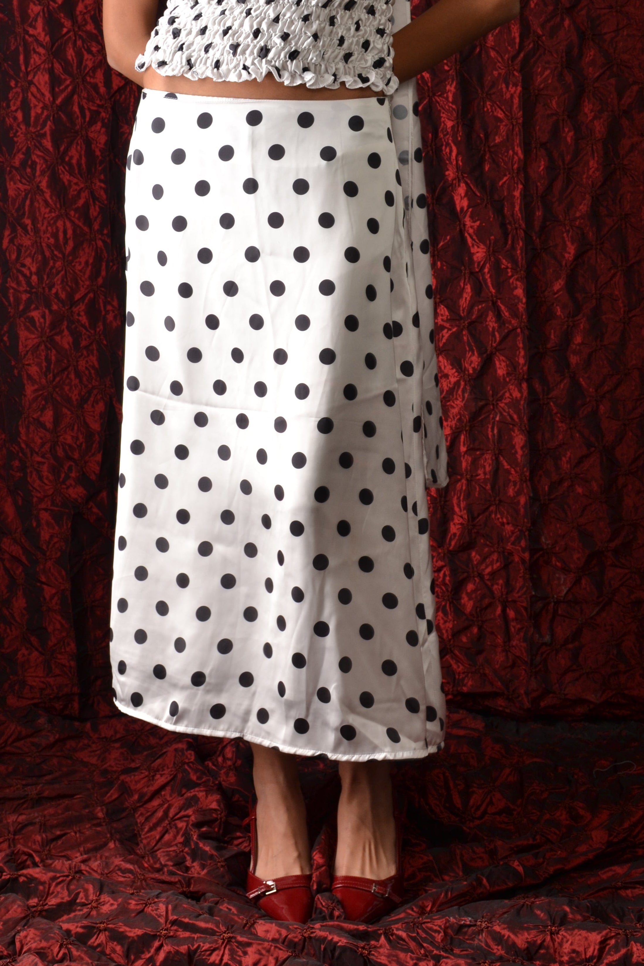 Person wearing a white dress with black polka dots lying on a red textured surface